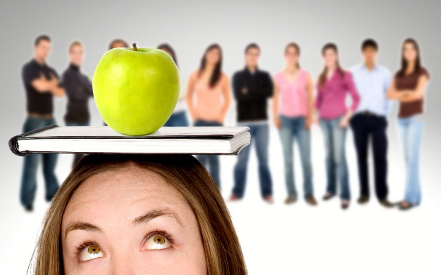 Rekrutacja - Dzewczyna z książką na głowie na któryej leży zielone jabłko, w tle ludzie